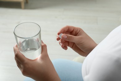 Photo of Woman with glass of water and pill on light background, closeup