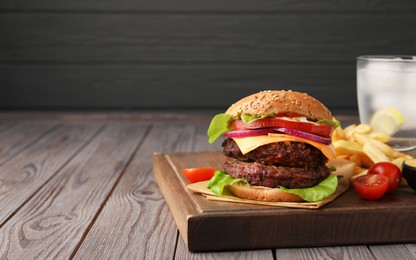 Tasty cheeseburger with patties, French fries and tomatoes on wooden table. Space for text