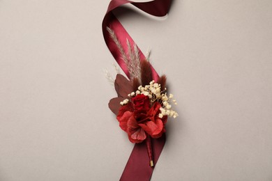 Stylish boutonniere and red ribbon on light grey background, top view