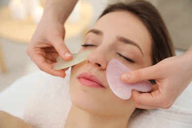 Photo of Young woman receiving facial massage with gua sha tools in beauty salon, closeup