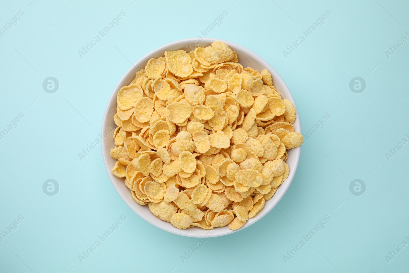 Photo of Breakfast cereal. Tasty corn flakes in bowl on light blue table, top view