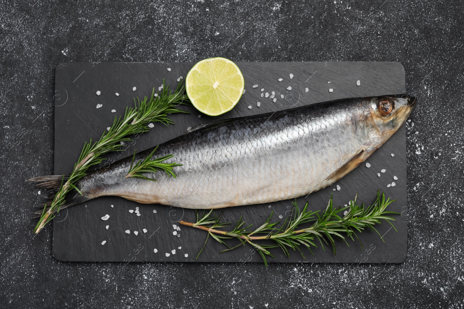 Photo of Delicious salted herring, rosemary and lemon on dark grey table, top view