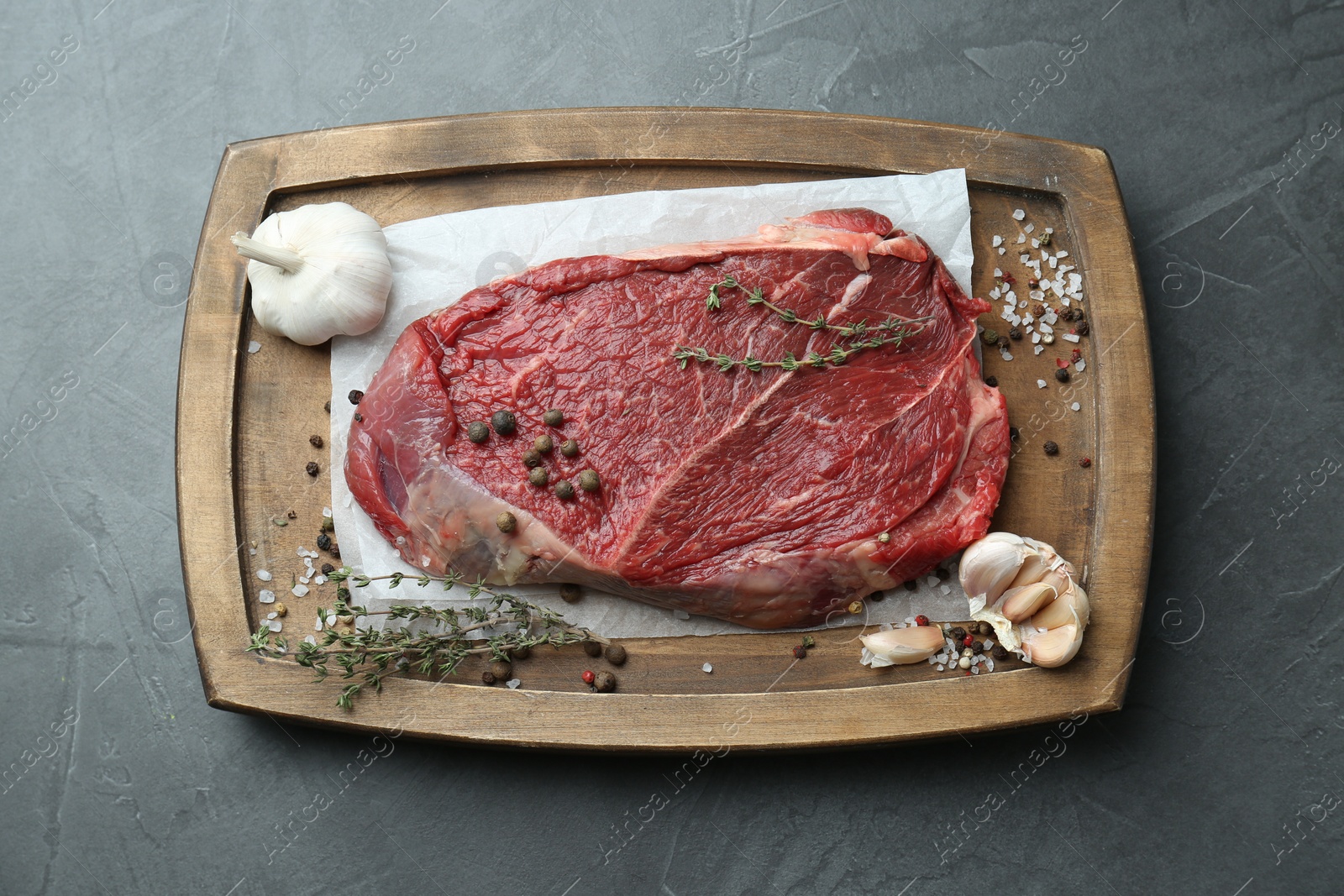 Photo of Wooden tray with piece of raw meat, garlic and thyme on grey table, top view