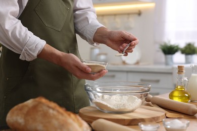 Making bread. Man putting dry yeast into bowl with flour at wooden table in kitchen, closeup