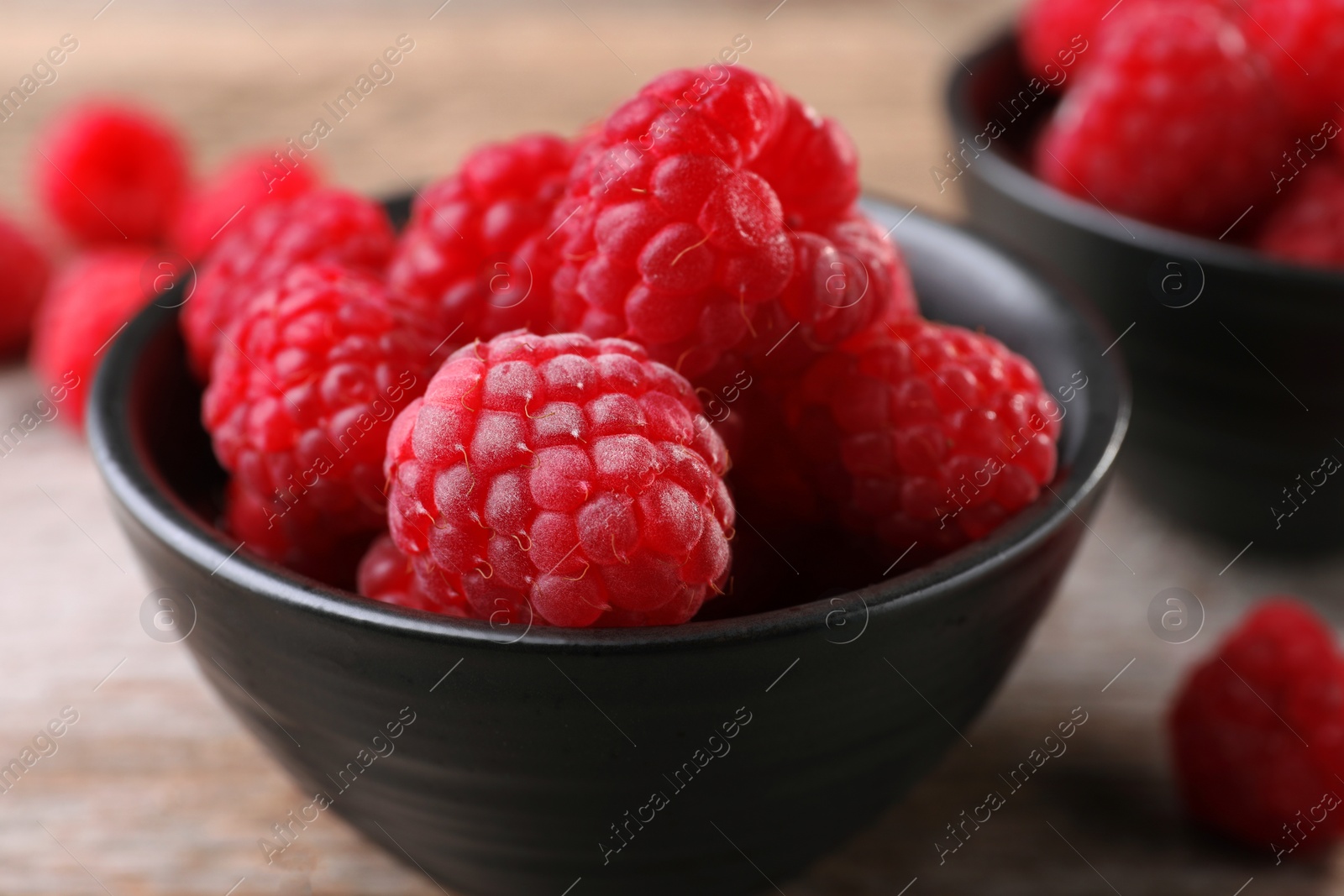 Photo of Tasty ripe raspberries in bowl on wooden table, closeup