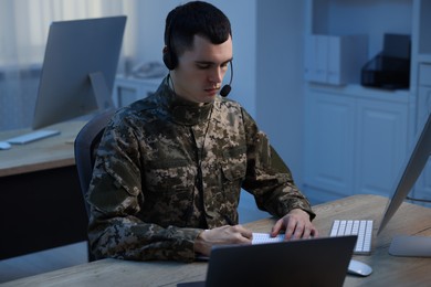 Military service. Young soldier in headphones working at wooden table in office at night