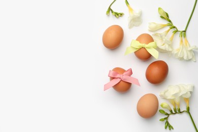 Easter eggs with colorful bows and flowers on white background, flat lay. Space for text