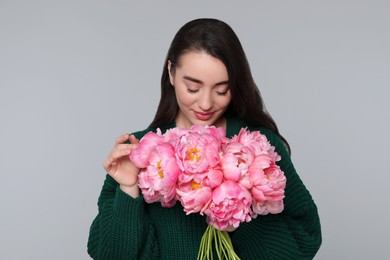 Photo of Beautiful young woman with bouquet of peonies on light grey background