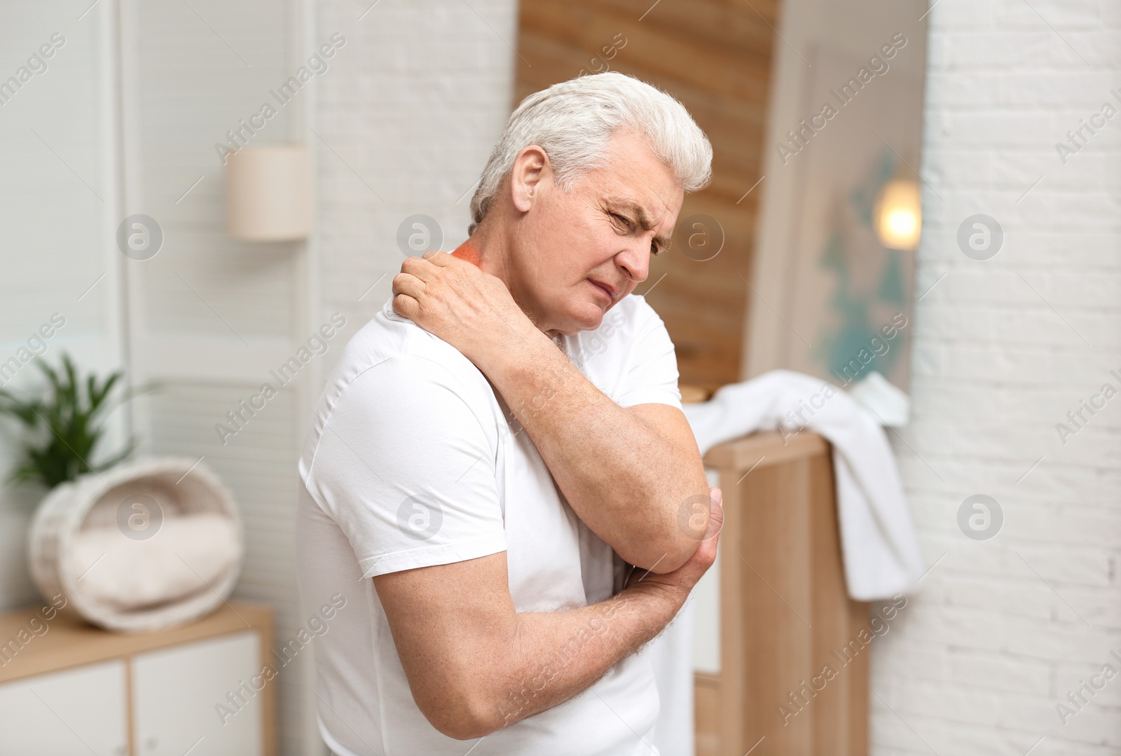 Photo of Senior man scratching neck indoors. Allergy symptom