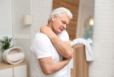 Photo of Senior man scratching neck indoors. Allergy symptom