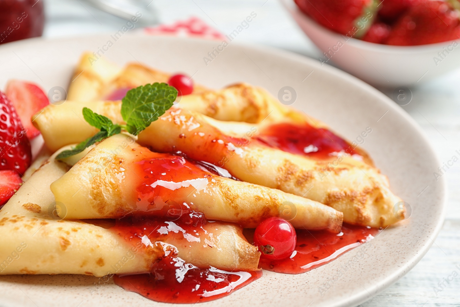 Photo of Delicious thin pancakes with strawberries and jam on plate, closeup