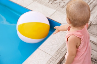 Photo of Little baby reaching for inflatable ball at outdoor swimming pool. Dangerous situation