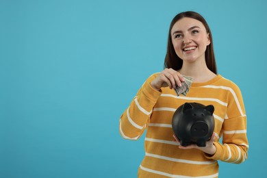 Happy woman putting dollar banknotes into piggy bank on light blue background, space for text