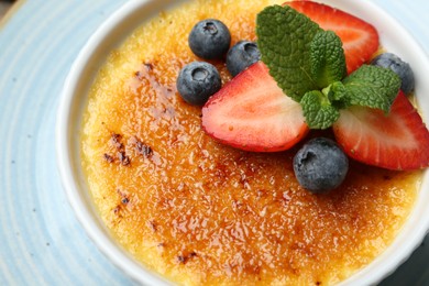 Photo of Delicious creme brulee with berries and mint in bowl on plate, above view