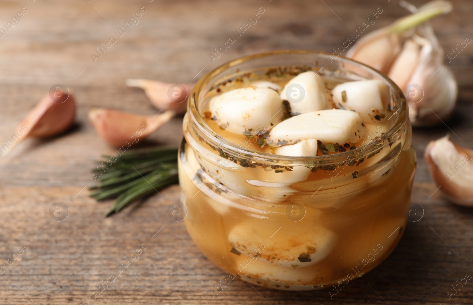 Photo of Preserved garlic in glass jar on wooden table, closeup