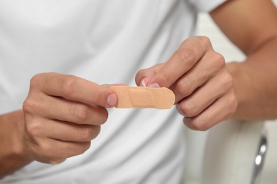 Photo of Young man opening sticking plaster, closeup view