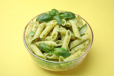 Photo of Delicious pasta with pesto sauce and basil on yellow background, closeup