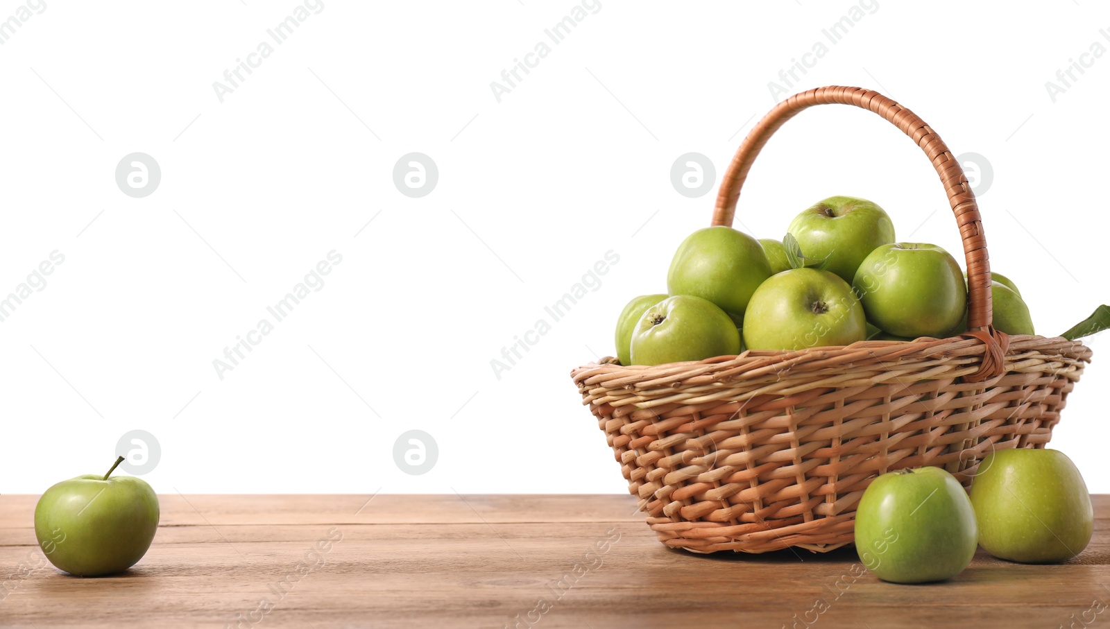 Photo of Ripe green apples in wicker basket on wooden table against white background. Space for text