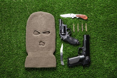 Flat lay composition with balaclava and weapons on green grass