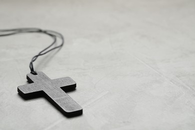 Wooden Christian cross on light grey table, closeup. Space for text