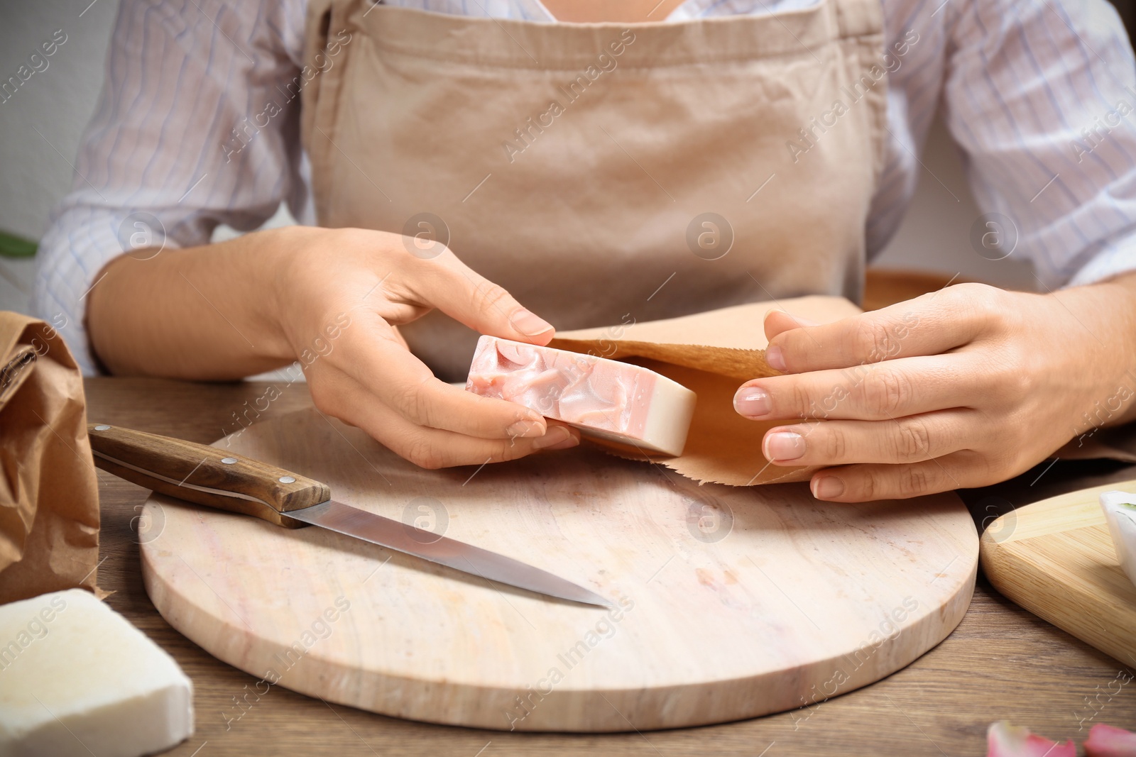 Photo of Woman putting natural handmade soap into paper bag at wooden table, closeup