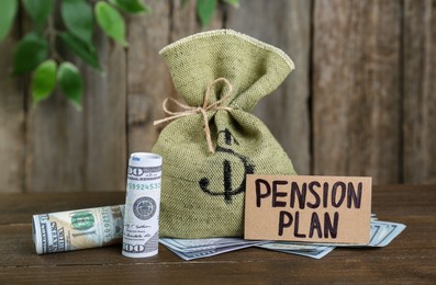 Card with phrase Pension Plan, dollar banknotes and sack on wooden table. Retirement concept