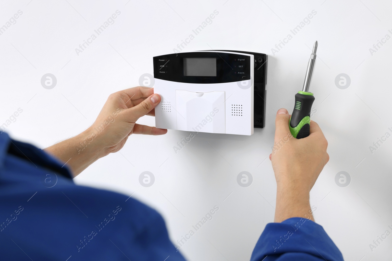 Photo of Man installing home security alarm system on white wall indoors, closeup