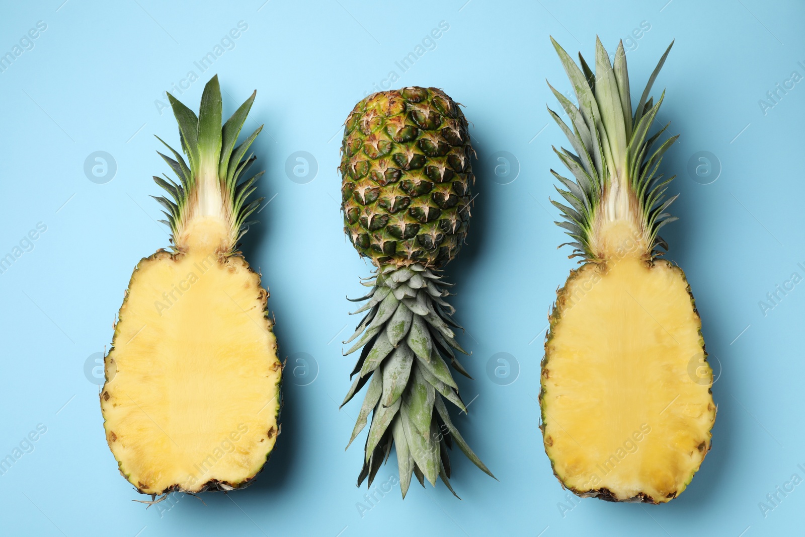 Photo of Fresh whole and cut pineapples on light blue background, top view