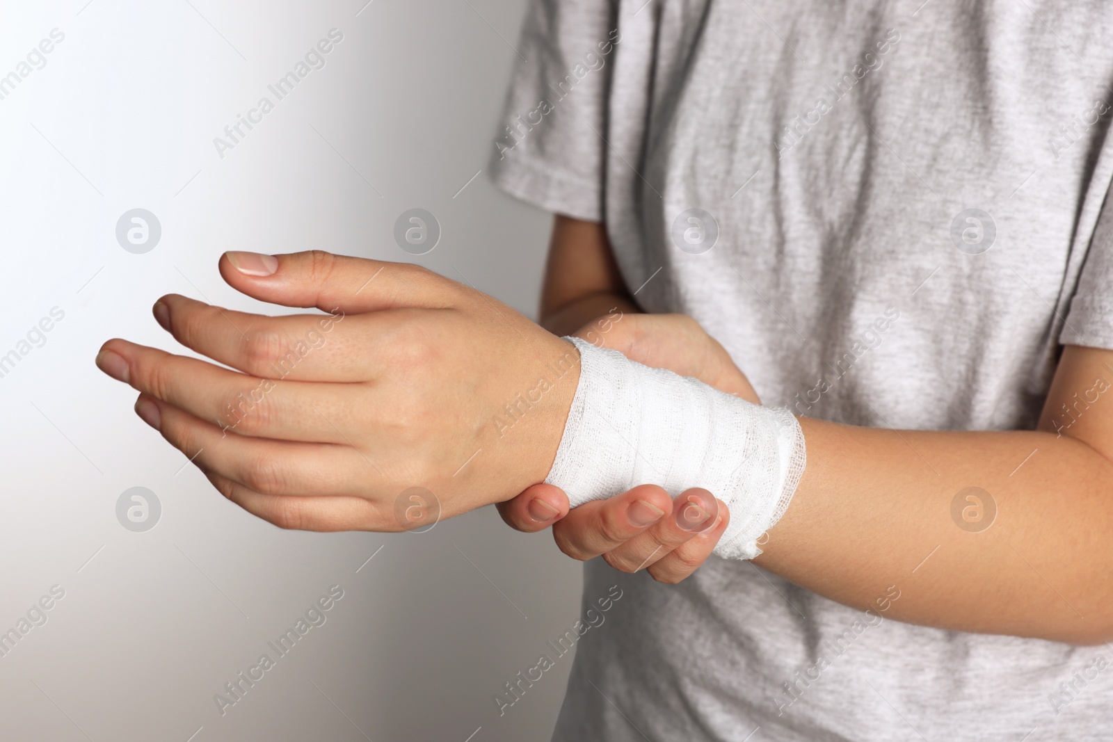 Photo of Woman with wrist wrapped in medical bandage on light grey background, closeup