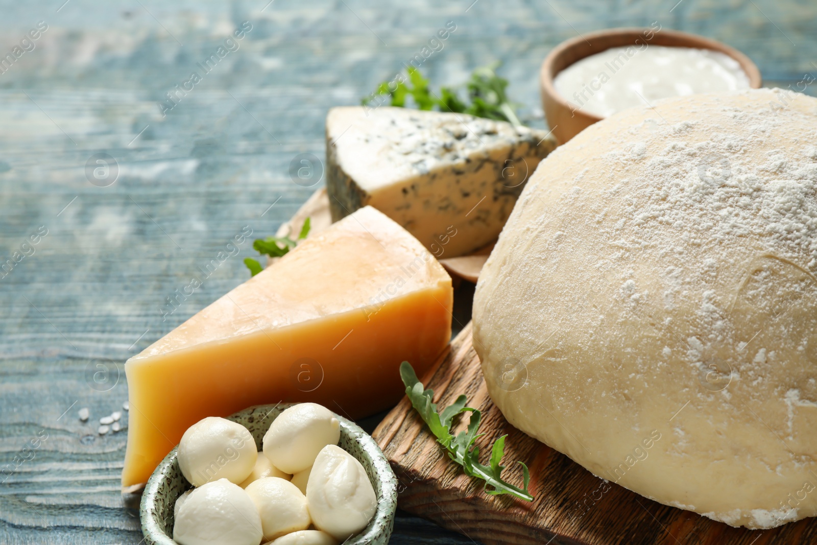 Photo of Fresh dough and pizza ingredients on blue wooden table, closeup