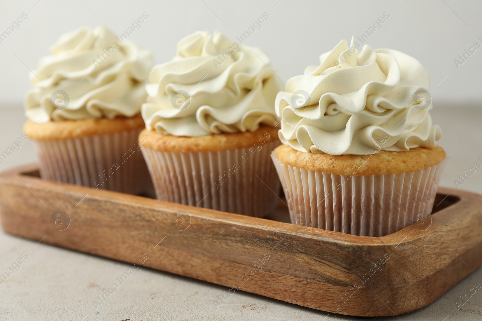 Photo of Tasty cupcakes with vanilla cream on light grey table, closeup