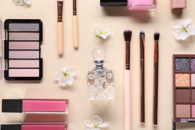 Photo of Flat lay composition with different makeup products and beautiful spring flowers on beige background