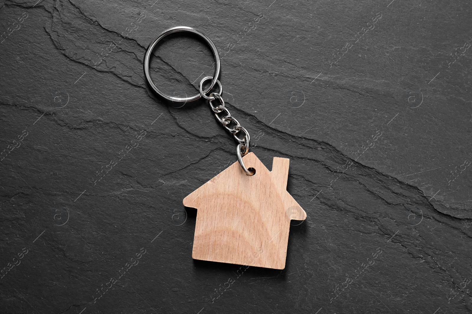 Photo of Wooden keychain in shape of house on dark textured table, top view