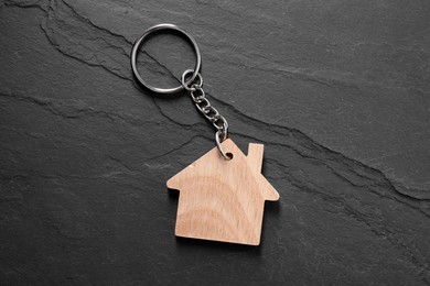 Photo of Wooden keychain in shape of house on dark textured table, top view