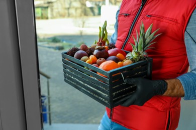 Courier holding crate with assortment of exotic fruits outdoors, closeup