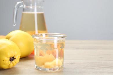 Photo of Delicious quince drink in glass and fresh fruits on wooden table, space for text