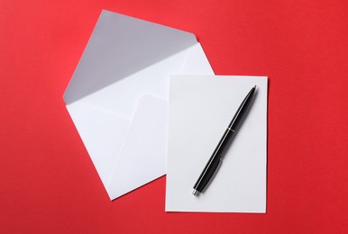 Blank sheet of paper, letter envelope and pen on red background, top view