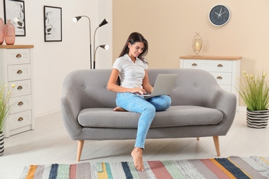 Beautiful woman with laptop sitting on sofa at home