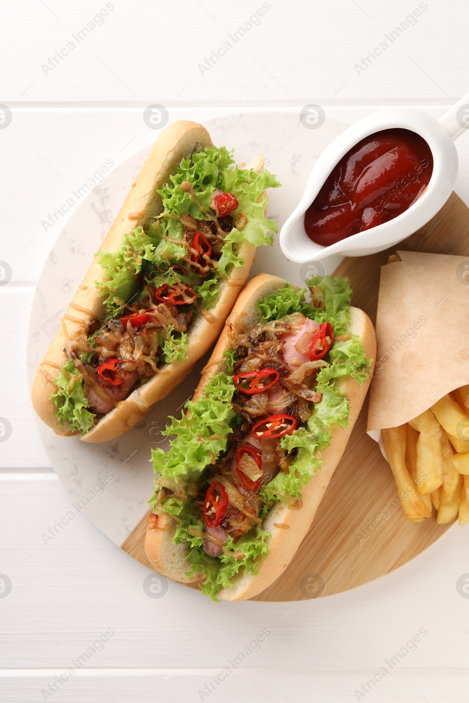 Photo of Tasty hot dogs with chili, lettuce, ketchup and French fries on white wooden table, top view