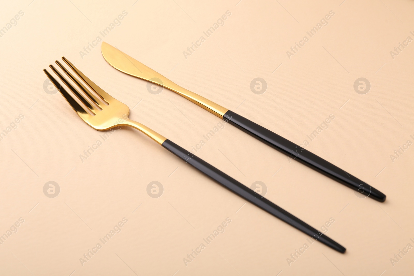 Photo of Stylish cutlery. Golden knife and fork on beige background