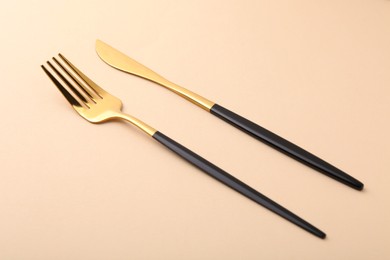 Photo of Stylish cutlery. Golden knife and fork on beige background