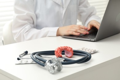 Photo of Endocrinologist working at table, focus on stethoscope and model of thyroid gland