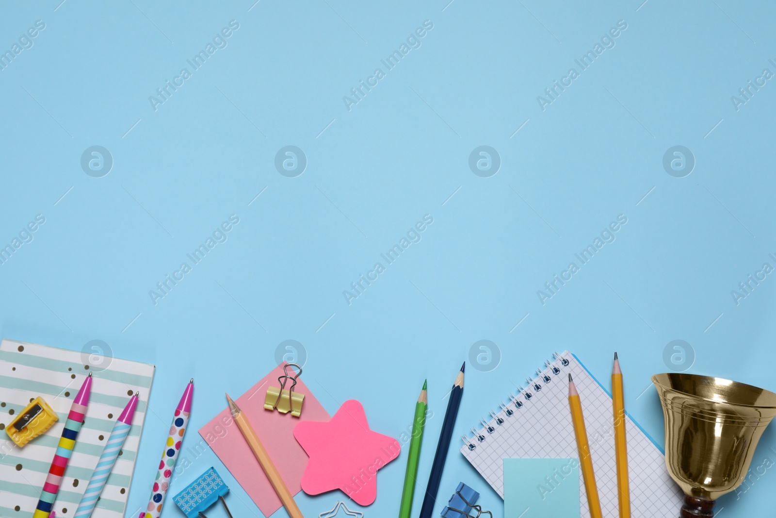 Photo of Different stationery and school bell on light blue background, flat lay. Space for text