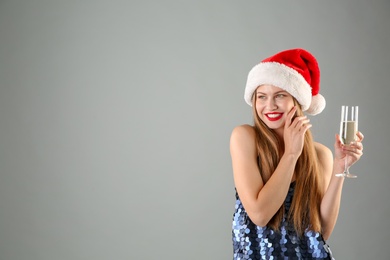 Young beautiful woman in Santa hat with glass of champagne on grey background. Christmas celebration