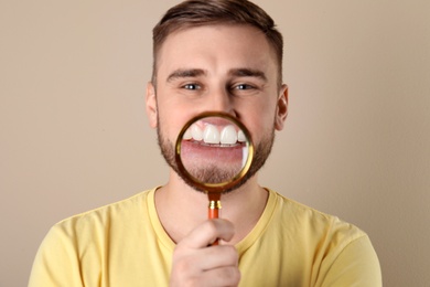 Photo of Young man with healthy teeth and magnifier on color background