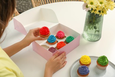 Woman with box of delicious colorful cupcakes at white table indoors, closeup