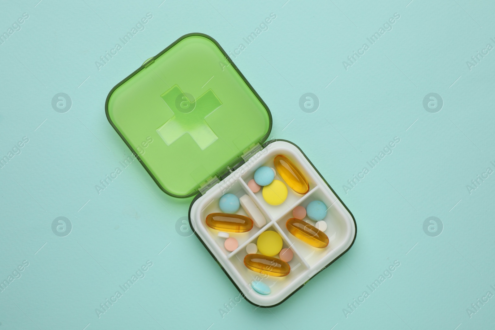 Photo of Plastic box with different pills on light blue background, top view