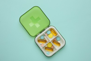 Plastic box with different pills on light blue background, top view