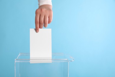 Photo of Woman putting her vote into ballot box on light blue background, closeup. Space for text