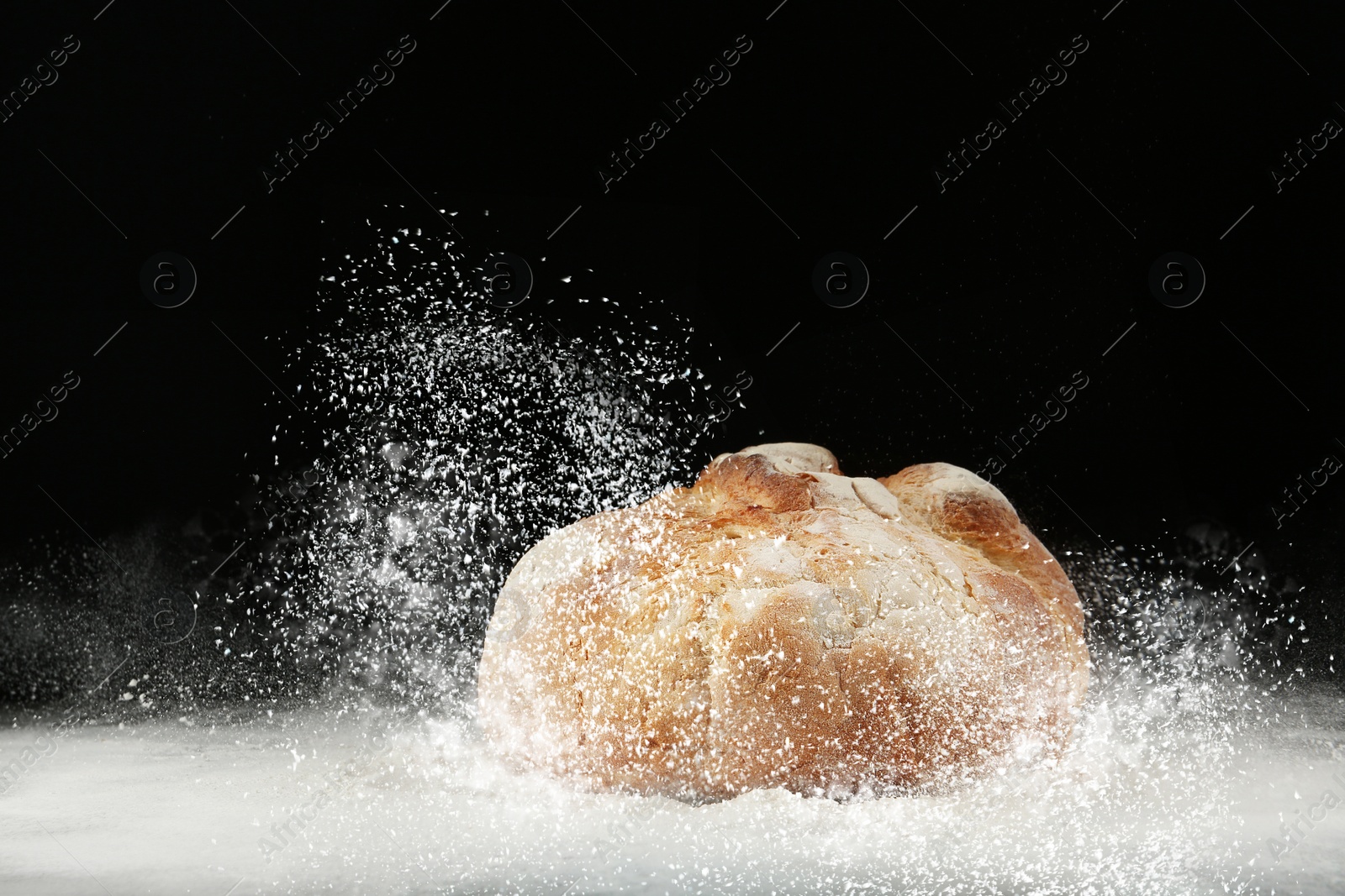 Image of Loaf of bread and flour on table against dark background